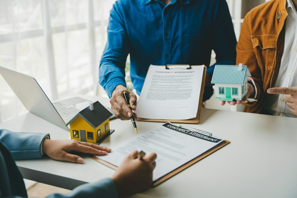 Un agente immobiliare consegna ai clienti campioni di case, discutendo i contratti di mutuo e preparando una proposta di locazione.
